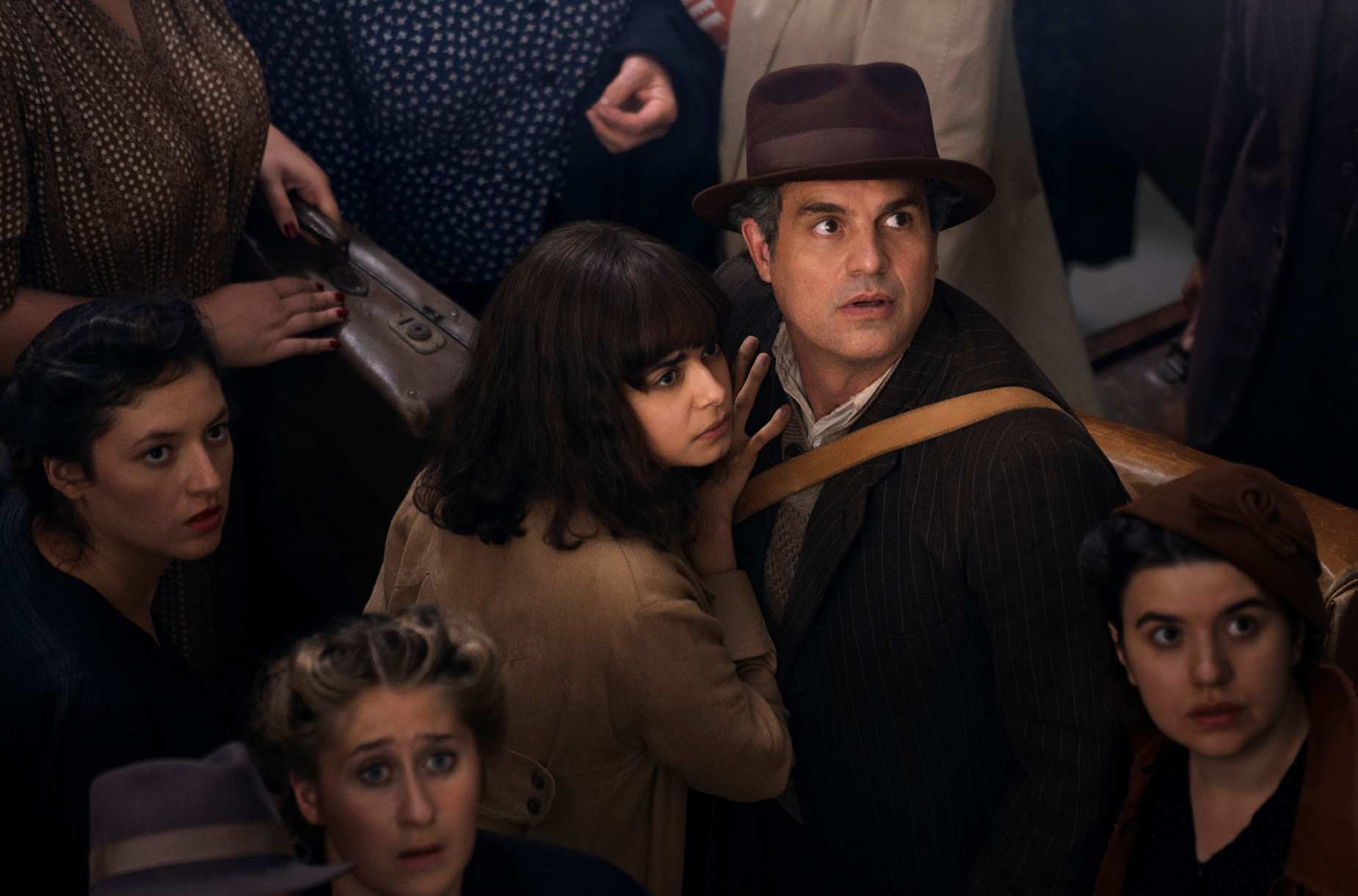 Imagem da série Toda Luz que Não Podemos Ver, da Netflix , com o ator Mark Ruffallo olhando para o alto em meio a várias mulheres